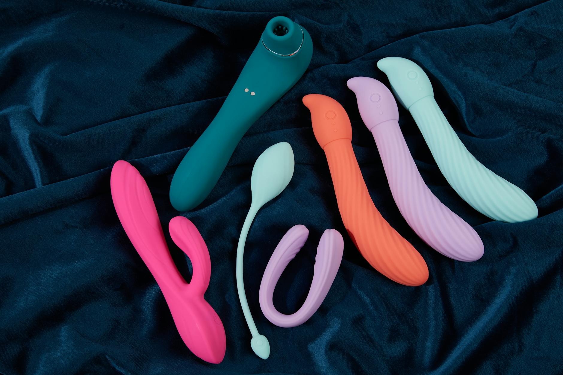 Una colección vibrante de juguetes sexuales de silicona en tela azul oscuro, mostrando diversos colores y formas