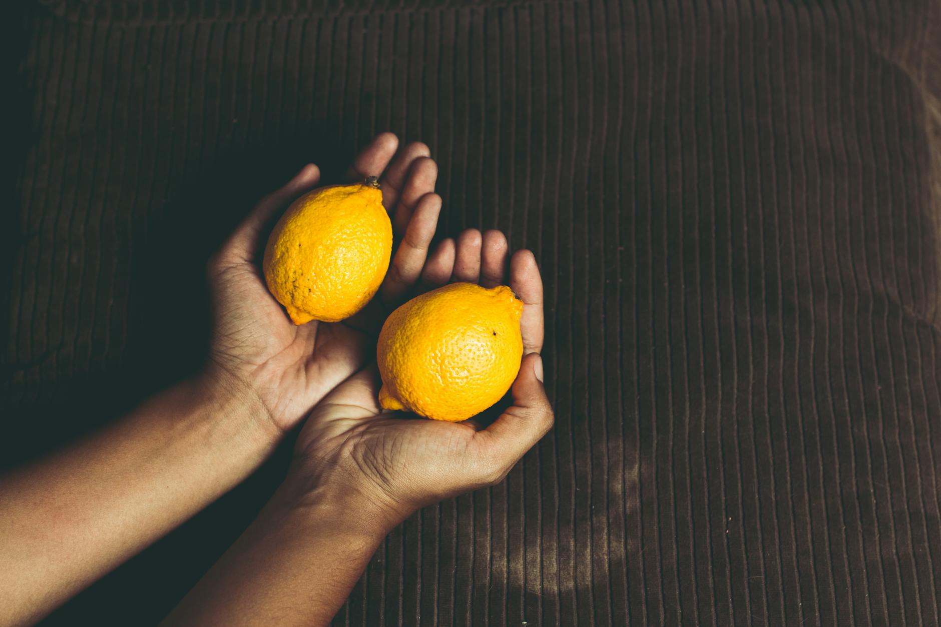 Dos limones frescos en las manos sobre una superficie marrón, simbolizando frescura y cuidado