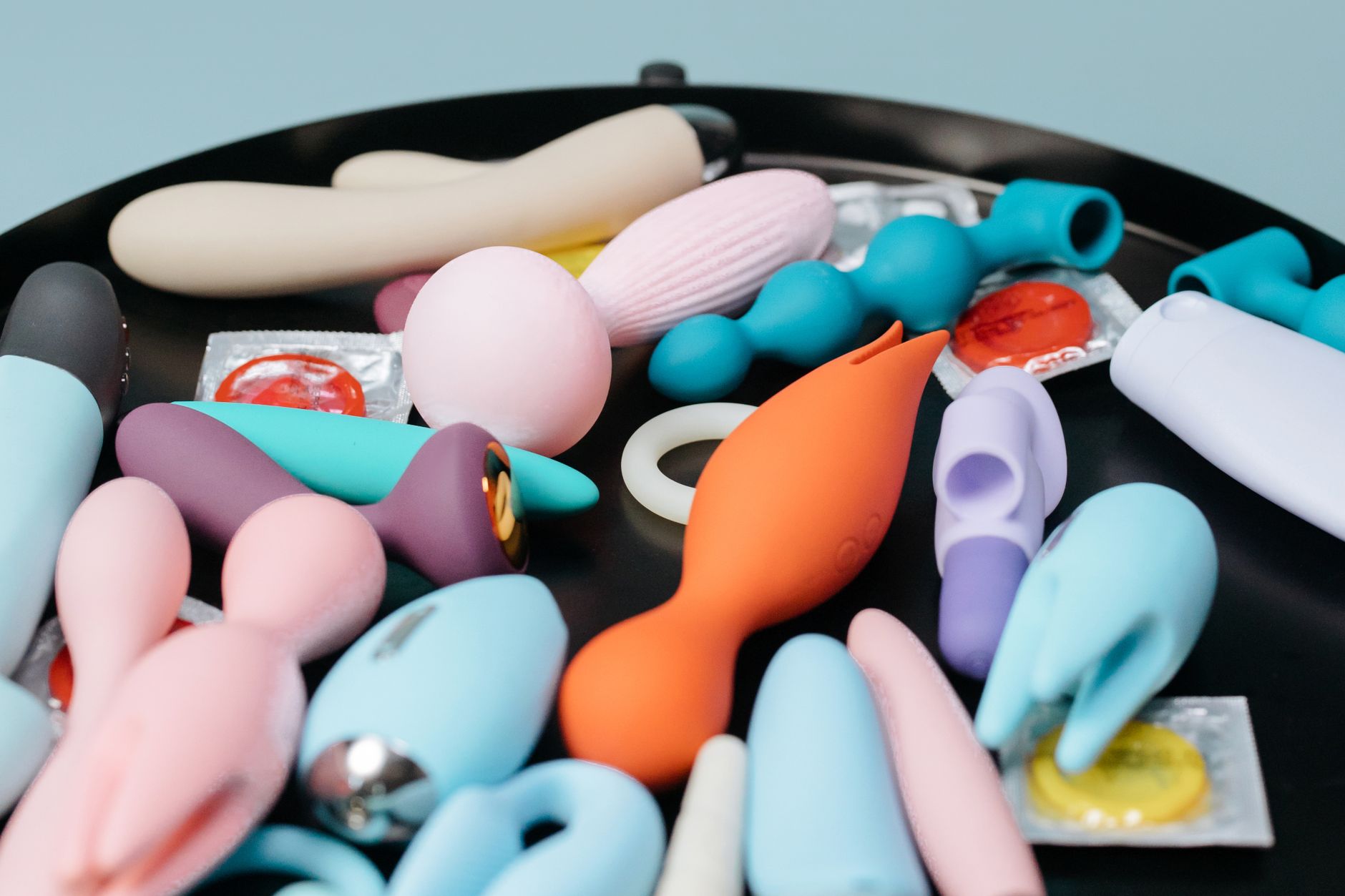 Hand reaching over a variety of colorful sex toys on a table, representing options for intimate connection