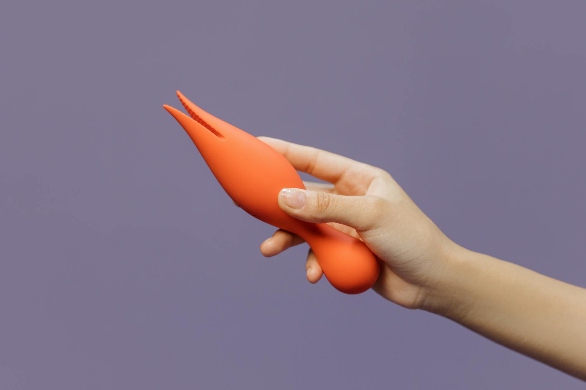 Close-up of a hand holding an orange vibrator against a minimalistic backdrop, showcasing modern sensuality.