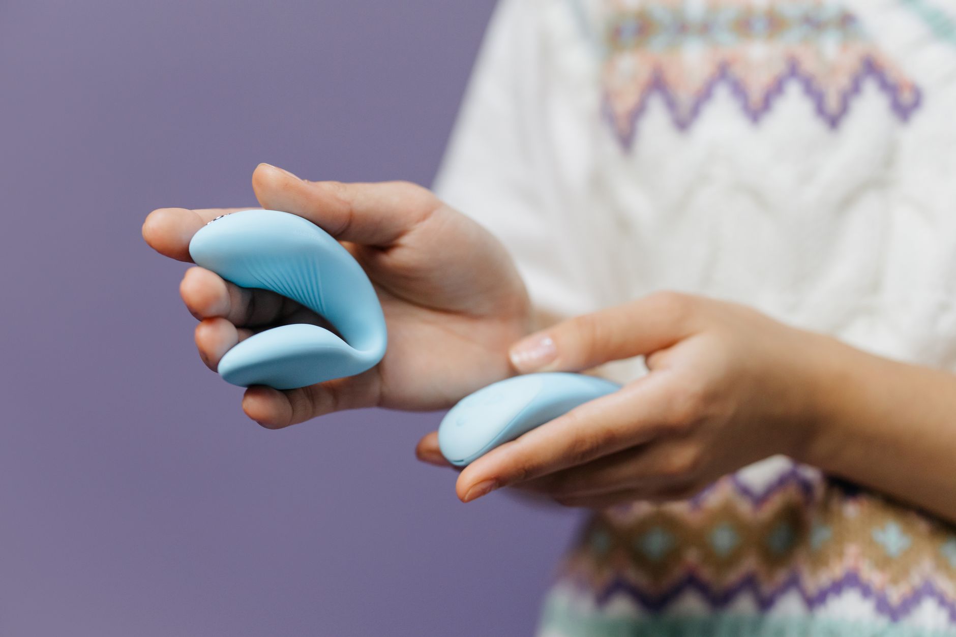 A hand holding a sleek blue clitoral vibrator against a purple background