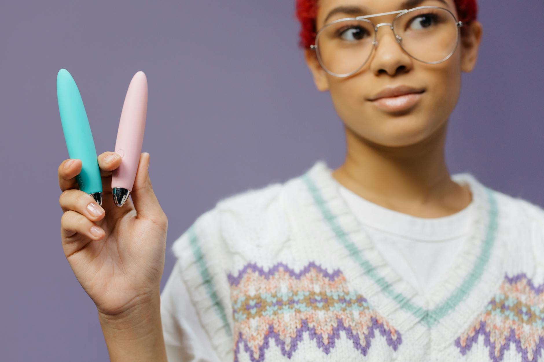 Woman with glasses holding colorful vibrators against a purple background, representing choice and self-care during recovery