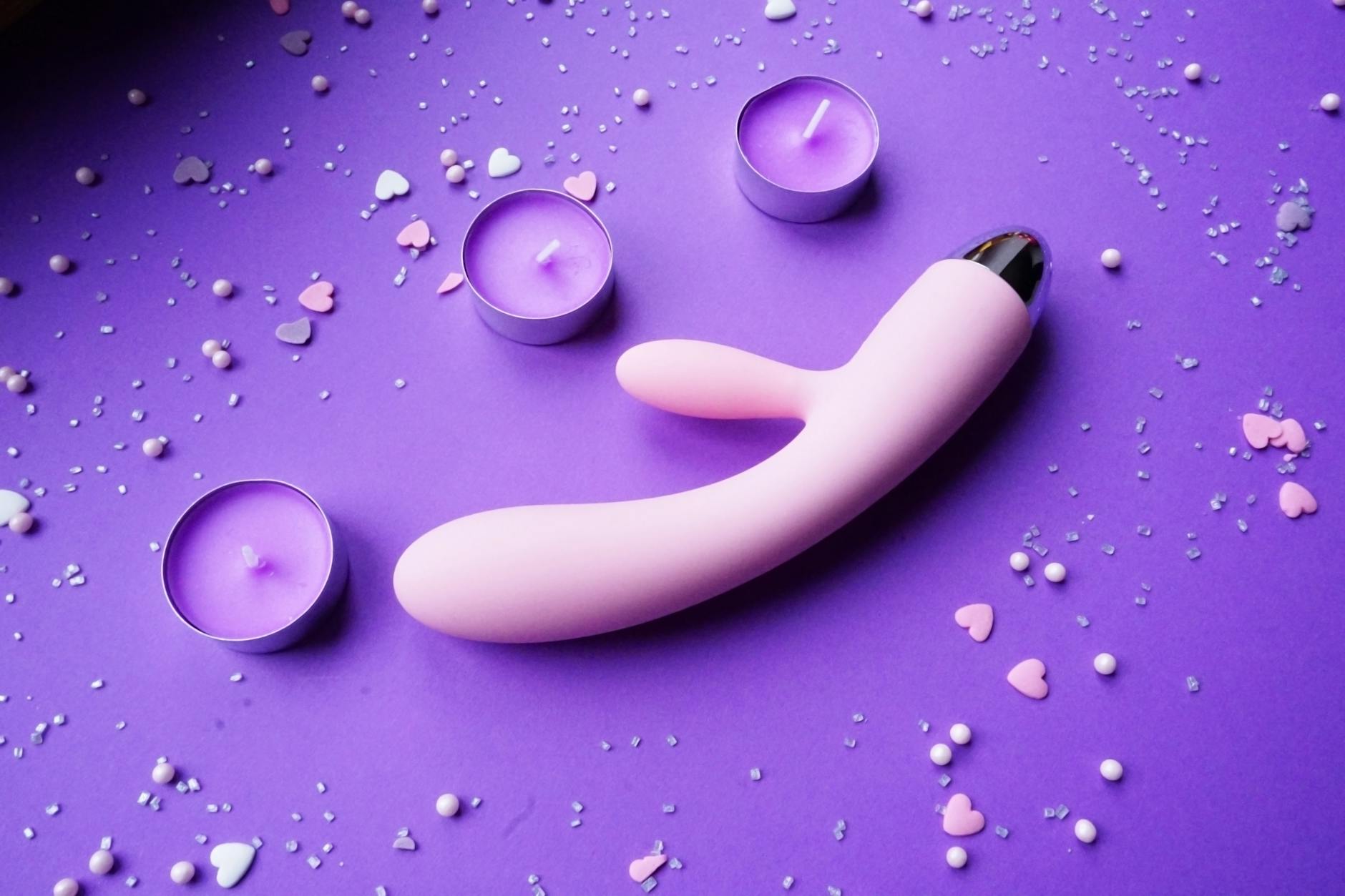 Pink lemon vibrator on purple background with heart confetti and candles in soft romantic lighting